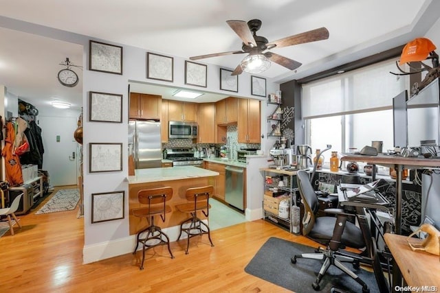 kitchen featuring appliances with stainless steel finishes, backsplash, light hardwood / wood-style floors, and ceiling fan