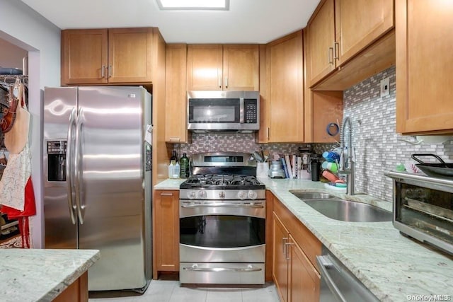 kitchen featuring backsplash, light stone countertops, sink, and appliances with stainless steel finishes