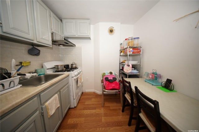 kitchen featuring sink, hardwood / wood-style floors, extractor fan, decorative backsplash, and white gas range oven