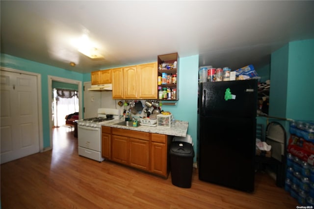 kitchen with light wood-type flooring, black fridge, white gas stove, and sink