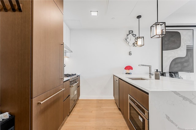 kitchen featuring sink, stainless steel appliances, hanging light fixtures, light stone counters, and light hardwood / wood-style flooring