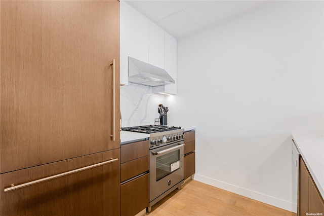 kitchen with white cabinetry, high end stainless steel range oven, extractor fan, decorative backsplash, and light wood-type flooring