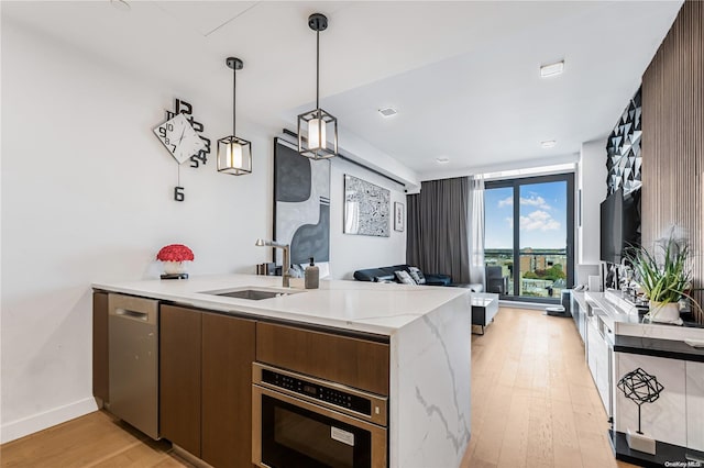 kitchen featuring kitchen peninsula, stainless steel appliances, sink, decorative light fixtures, and light hardwood / wood-style floors