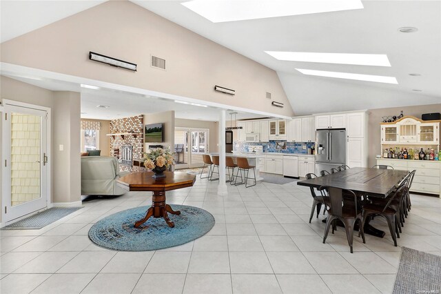 dining area with light tile patterned flooring, a fireplace, high vaulted ceiling, and a skylight