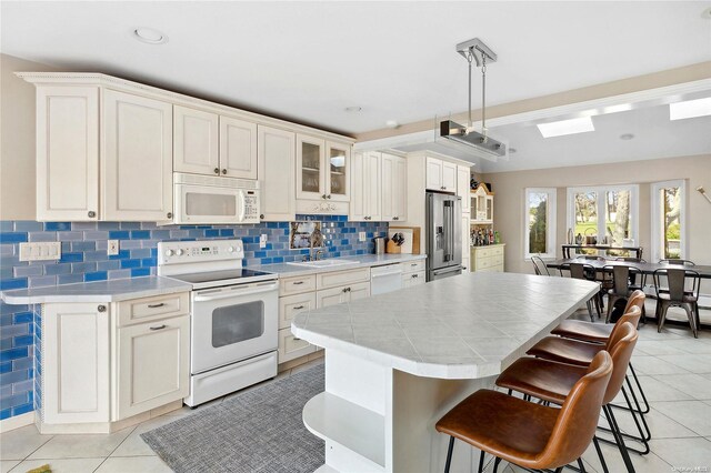 kitchen with white cabinets, light tile patterned flooring, white appliances, and sink