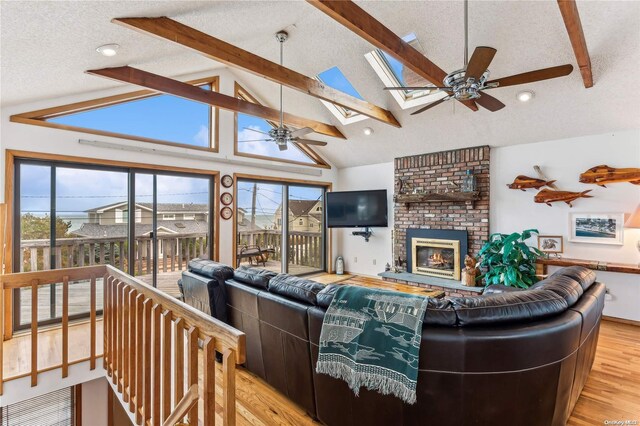 living room with a brick fireplace, vaulted ceiling with skylight, a textured ceiling, and light wood-type flooring