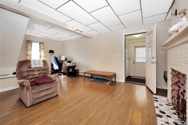 living area featuring a baseboard heating unit, hardwood / wood-style flooring, a brick fireplace, and a healthy amount of sunlight