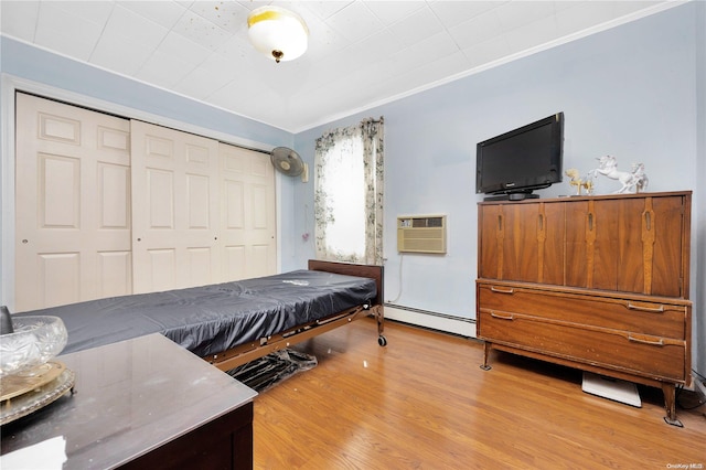 bedroom featuring ornamental molding, a baseboard radiator, light hardwood / wood-style floors, a wall unit AC, and a closet