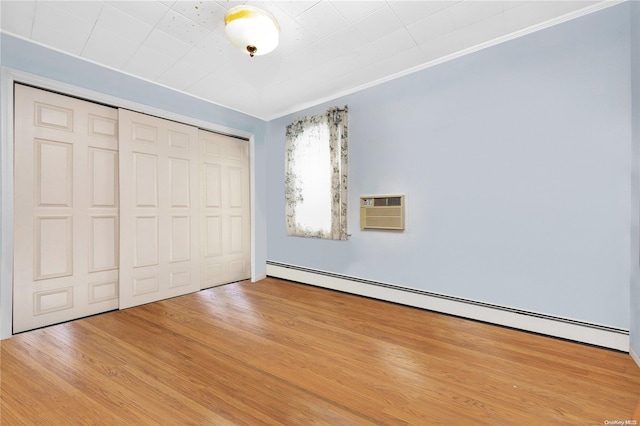 unfurnished bedroom with a baseboard radiator, a wall unit AC, hardwood / wood-style flooring, a closet, and ornamental molding