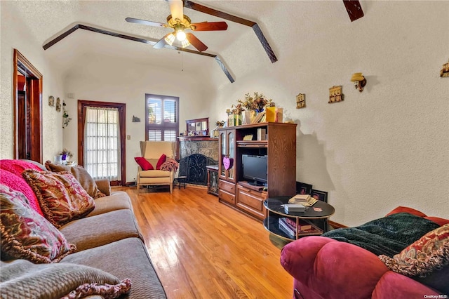 living room featuring hardwood / wood-style flooring, ceiling fan, a stone fireplace, and a textured ceiling