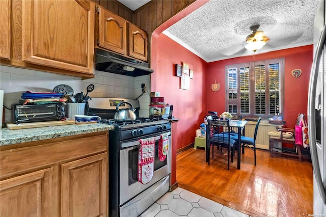 kitchen with stainless steel gas stove, a textured ceiling, range hood, tasteful backsplash, and light hardwood / wood-style floors