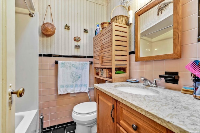 bathroom with vanity, a bathtub, toilet, and tile walls