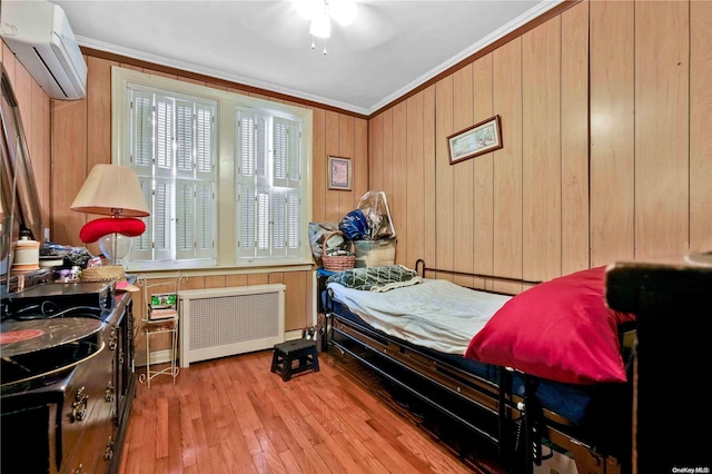 bedroom featuring ceiling fan, radiator heating unit, a wall unit AC, light wood-type flooring, and ornamental molding