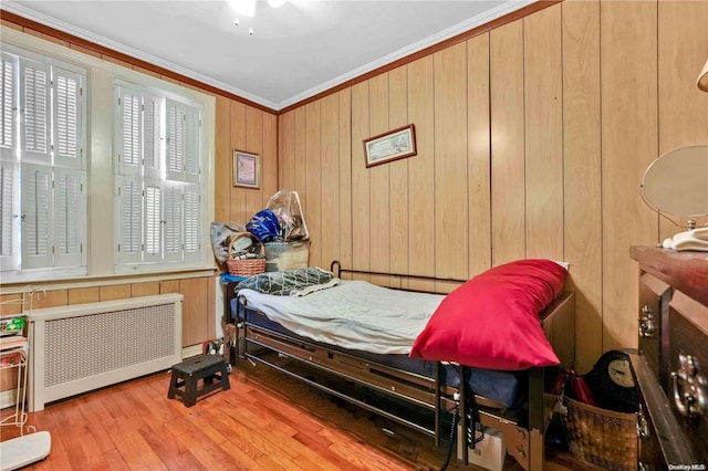 bedroom featuring wooden walls, ceiling fan, light wood-type flooring, ornamental molding, and radiator heating unit