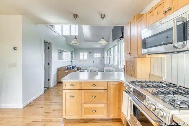 kitchen featuring light brown cabinets, kitchen peninsula, decorative light fixtures, appliances with stainless steel finishes, and light wood-type flooring