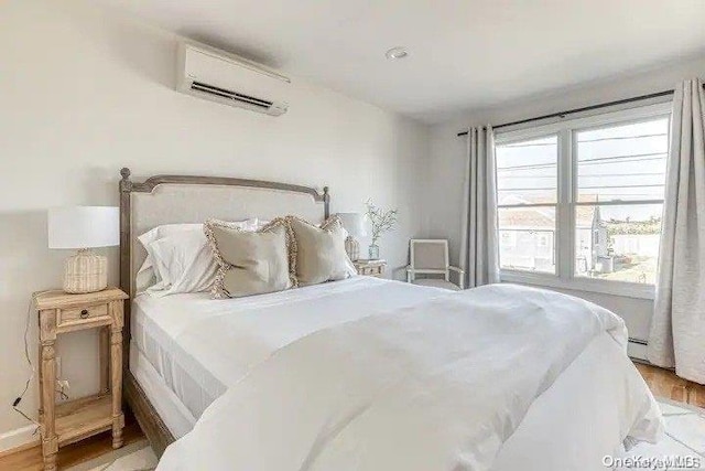 bedroom featuring a wall mounted air conditioner, light hardwood / wood-style floors, and baseboard heating