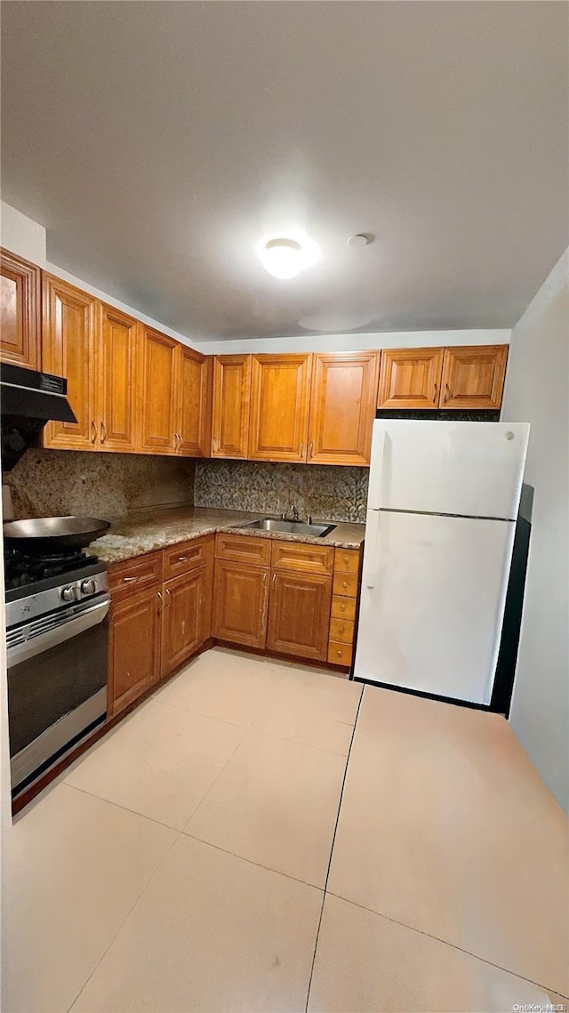 kitchen with white refrigerator, sink, decorative backsplash, stainless steel range, and light tile patterned flooring