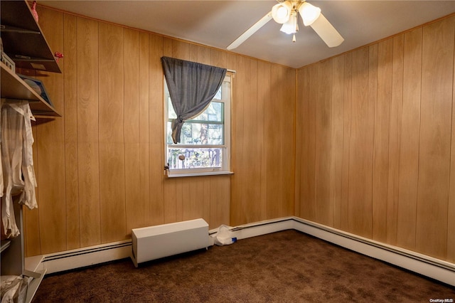 spare room featuring dark colored carpet, baseboard heating, ceiling fan, and wood walls