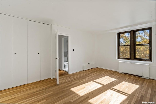 unfurnished bedroom with radiator heating unit, light hardwood / wood-style flooring, and a closet