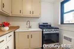 kitchen featuring decorative backsplash, radiator, and stainless steel range with gas stovetop