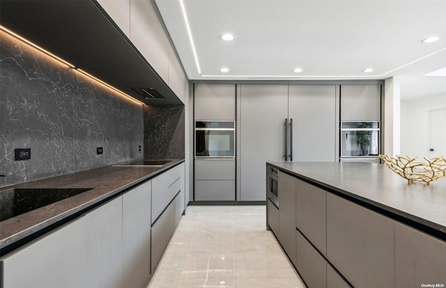 kitchen with tasteful backsplash, gray cabinetry, dark stone counters, and stainless steel appliances