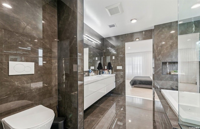 bathroom featuring vanity, toilet, tile walls, and tiled tub