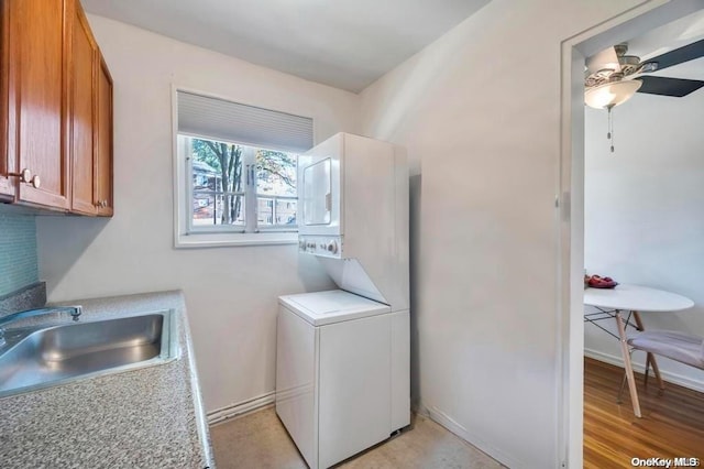 laundry area with ceiling fan, light hardwood / wood-style flooring, stacked washer / drying machine, and sink