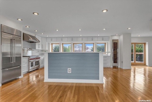 kitchen with light hardwood / wood-style flooring, white cabinets, wall chimney range hood, and premium appliances