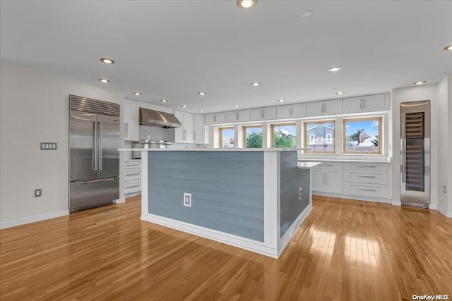 kitchen featuring white cabinetry, a center island, wall chimney exhaust hood, light hardwood / wood-style flooring, and stainless steel built in fridge