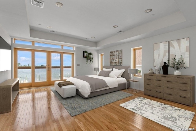 bedroom featuring multiple windows, light hardwood / wood-style flooring, and a water view