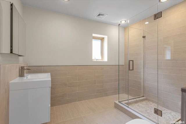 bathroom with tile patterned floors, vanity, tile walls, and walk in shower