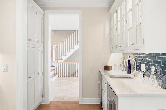 kitchen with white cabinetry, sink, light hardwood / wood-style flooring, backsplash, and crown molding