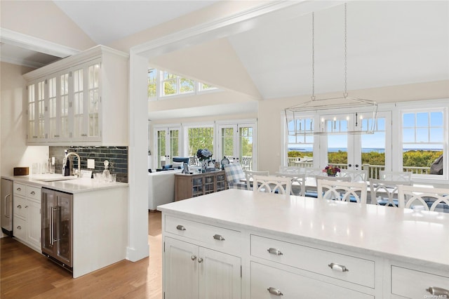 kitchen with pendant lighting, white cabinets, sink, wine cooler, and light wood-type flooring