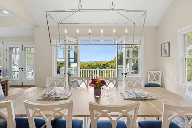 dining space with hardwood / wood-style flooring, vaulted ceiling, an inviting chandelier, and french doors