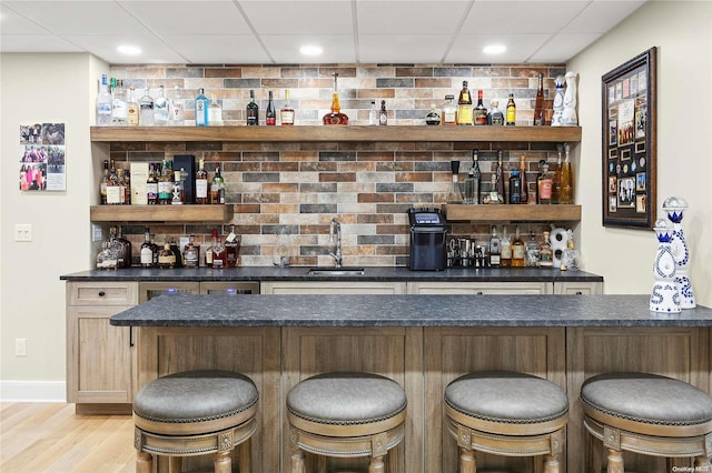 bar featuring light wood-type flooring, backsplash, a paneled ceiling, and sink