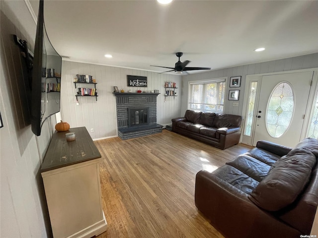 living room with hardwood / wood-style floors, ceiling fan, a fireplace, and wooden walls