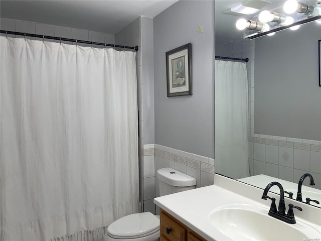 bathroom with curtained shower, vanity, tile walls, and toilet