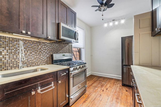 kitchen with appliances with stainless steel finishes, backsplash, ceiling fan, sink, and light hardwood / wood-style floors