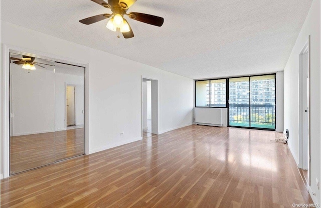 unfurnished room with ceiling fan, expansive windows, a textured ceiling, and light hardwood / wood-style flooring