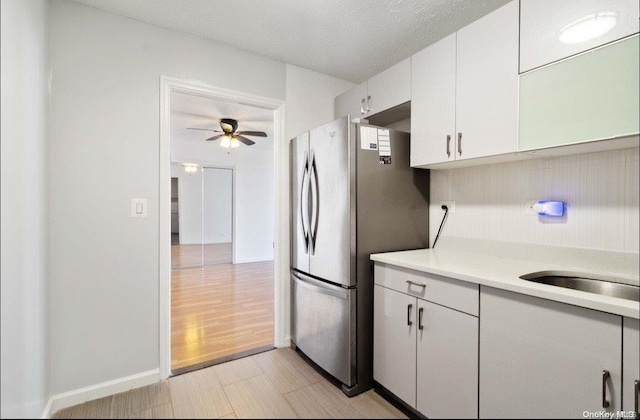 kitchen with a textured ceiling, ceiling fan, light hardwood / wood-style flooring, white cabinets, and stainless steel refrigerator