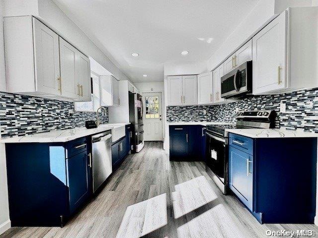 kitchen featuring white cabinetry, blue cabinets, backsplash, appliances with stainless steel finishes, and light wood-type flooring