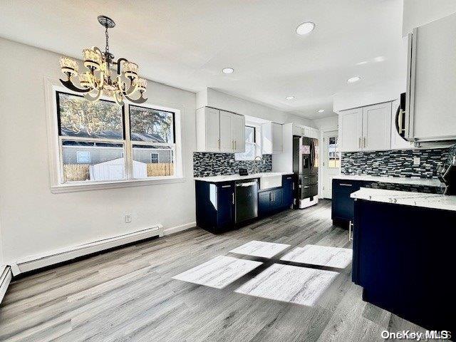 kitchen with appliances with stainless steel finishes, backsplash, light hardwood / wood-style flooring, a chandelier, and white cabinetry