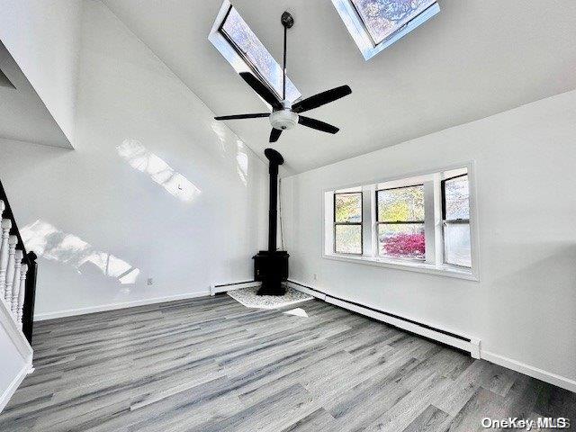 unfurnished living room featuring lofted ceiling with skylight, ceiling fan, wood-type flooring, and a baseboard heating unit