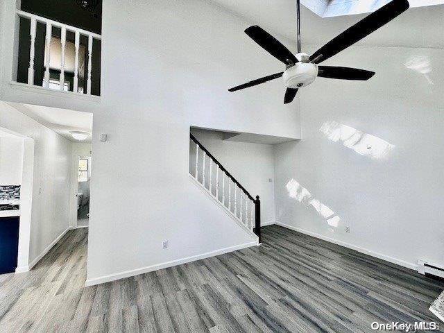 unfurnished living room with wood-type flooring, ceiling fan, a baseboard heating unit, and a high ceiling