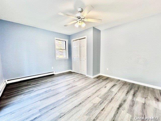 unfurnished bedroom with ceiling fan, a closet, a baseboard radiator, and light hardwood / wood-style floors