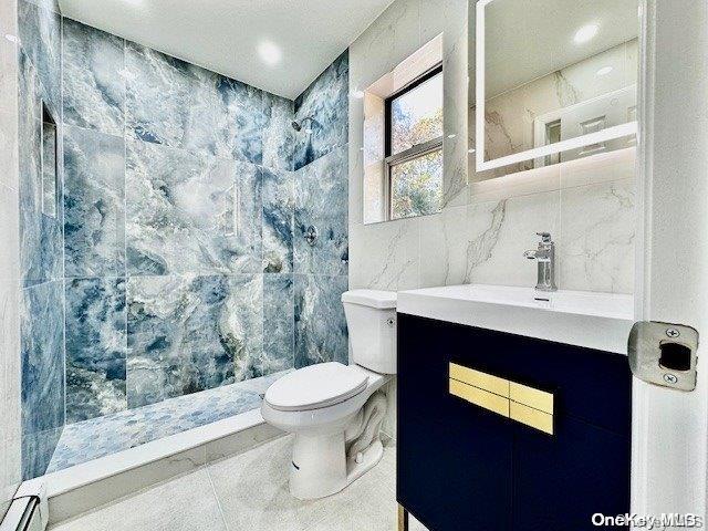 bathroom with tile patterned floors, vanity, a shower, tile walls, and toilet