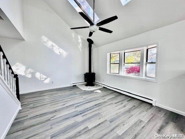 unfurnished living room with ceiling fan, wood-type flooring, and a baseboard heating unit