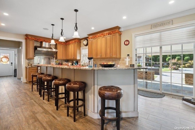 kitchen with wall chimney range hood, crown molding, decorative backsplash, light wood-type flooring, and kitchen peninsula