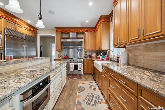 kitchen featuring sink, decorative light fixtures, wall chimney exhaust hood, light wood-type flooring, and premium appliances