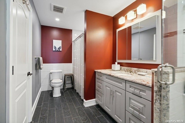 bathroom featuring walk in shower, vanity, tile walls, and toilet